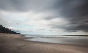 Spokojna plaża i morze, idealne na wypoczynek w ośrodku wczasowym Zacisze. Długie fale i las sosnowy tworzą malowniczy krajobraz.