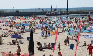 Tłum ludzi na plaży w Łebie. W tle widać morze i port. Tyle mieszkańców ma Łeba, że plaża jest tak pełna.