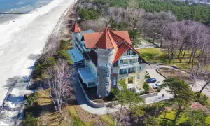 Elegancki hotel z wieżą i czerwonym dachem oferuje noclegi Łeba blisko morza. Piękna plaża i las otaczają obiekt.