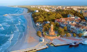 Widok na plażę, morze bałtyckie i latarnię morską. W tle hotel i zabudowania miejskie.