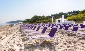 Rządki leżaków na piaszczystej plaży, idealne na tanie wczasy nad morzem dla 2 osób z wyżywieniem. W tle morze i zieleń.