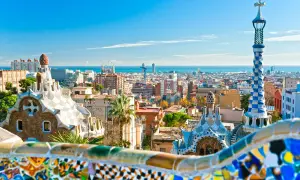 Widok na kolorowe budowle Parku Güell i panoramę miasta, gdzie leży Barcelona, z morzem w tle.