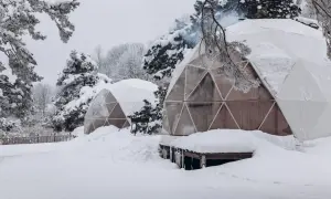 Śnieżne krajobrazy i przytulne domki do wynajęcia na weekend. Dym unosi się z komina jednego z igloo, zapraszając do środka.