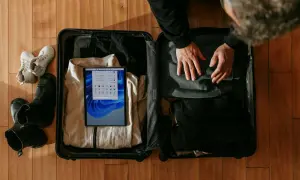 Osoba pakuje walizkę podręczną, w której widać ubrania, buty i tablet.