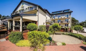 Hotel La Siesta w słoneczny dzień. Budynek z balkonami otoczony zielenią i brukowanym dziedzińcem.