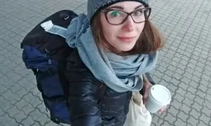 Kobieta w czapce i szaliku trzyma kubek kawy, obok plecak.