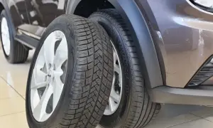 Dwa opony samochodowe, jeden całoroczny, drugi zimowy, obok brązowego samochodu.