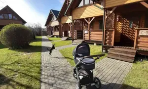 Wesoły piesek goni piłkę na ścieżce przy domkach w ośrodku wczasowym Sęk w Karwi. Obok stoi wózek dziecięcy.