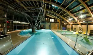 Wnętrze Laguna Kompleks Wypoczynkowo Rekreacyjny Mrzeżyno: baseny, jacuzzi, leżaki pod drewnianą, przeszkloną konstrukcją dachu.