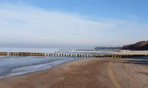 Spokojne morze i pusta plaża w Rusinowie nad morzem. Drewniane falochrony wcinają się w wodę, tworząc malowniczy krajobraz.