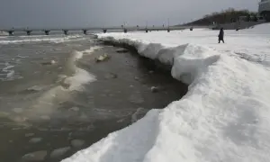Zimne morze z lodem i śniegiem na brzegu. W oddali widać molo i spacerujących ludzi. Czy morze zamarza? Tak, widać to wyraźnie.
