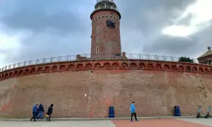 Latarnia morska w Kołobrzegu, jeden z punktów, które warto zobaczyć. Potężny ceglany fort i wieża górują nad spacerującymi.