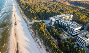 Nowoczesne budynki hotelowe w Rogowie nad morzem, otoczone sosnowym lasem, z widokiem na piaszczystą plażę i fale Bałtyku.