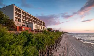 Idealne noclegi przy plaży z widokiem na morze. Hotel z balkonami wychodzącymi na piaszczystą plażę i spokojne morze o zachodzie słońca.