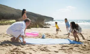 Rodzina cieszy się urlopem nad morzem. Dzieci biegają po plaży, a rodzice rozkładają ręcznik.