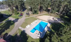 Mrzeżyno wczasy dla seniora: basen, leżaki i boisko do siatkówki w otoczeniu sosnowego lasu. Grupa osób na piasku.