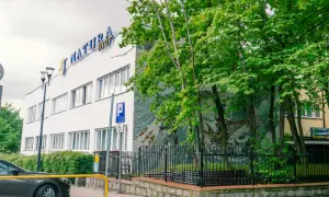 Dom wczasowy Radość, budynek z niebieskim napisem "NATURA tour", otoczony zielenią i ozdobiony mozaiką.