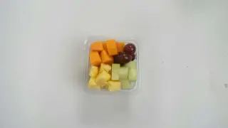 Pudełko z pokrojonymi owocami: ananas, melon, papaja i winogrona. Idealne na przekąskę w podróży, zastanawiasz się, czy można przewozić jedzenie w bagażu rejestrowanym?