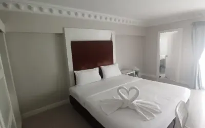 Elegancki pokój hotelowy z łóżkiem ozdobionym ręcznikami w kształcie łabędzi. Idealne miejsce, gdzie szukać noclegu na wakacje.