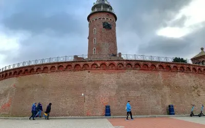 Latarnia morska w Kołobrzegu, jeden z punktów, które warto zobaczyć. Potężny ceglany fort i wieża górują nad spacerującymi.