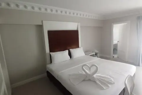Elegancki pokój hotelowy z łóżkiem ozdobionym ręcznikami w kształcie łabędzi. Idealne miejsce, gdzie szukać noclegu na wakacje.
