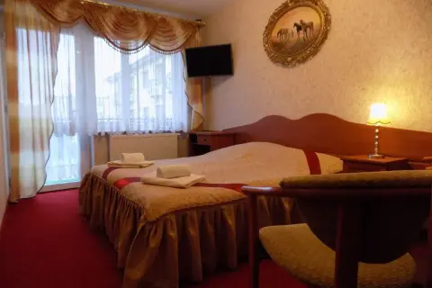 Przytulny pokój w pensjonacie Angela Łeba. Łóżko z czystymi ręcznikami, obraz z końmi i lampka nocna.
