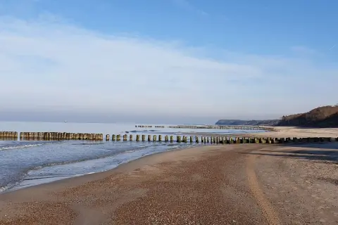 Spokojne morze i pusta plaża w Rusinowie nad morzem. Drewniane falochrony wcinają się w wodę, tworząc malowniczy krajobraz.