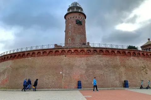 Latarnia morska w Kołobrzegu, jeden z punktów, które warto zobaczyć. Potężny ceglany fort i wieża górują nad spacerującymi.