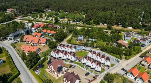 Widok z lotu ptaka na Dębki: domki z czerwonymi dachami, las i morze w tle.