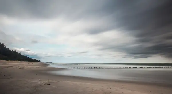 Spokojna plaża i morze, idealne na wypoczynek w ośrodku wczasowym Zacisze. Długie fale i las sosnowy tworzą malowniczy krajobraz.