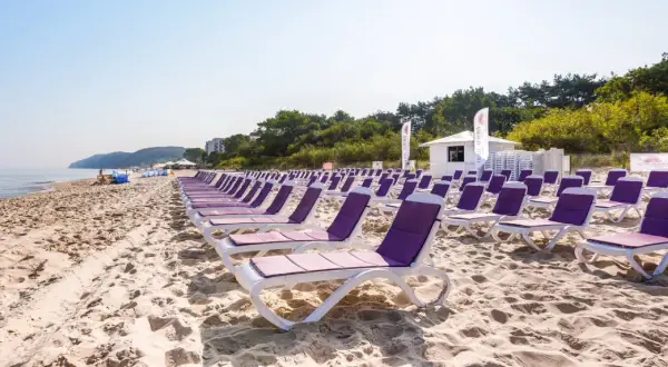 Rządki leżaków na piaszczystej plaży, idealne na tanie wczasy nad morzem dla 2 osób z wyżywieniem. W tle morze i zieleń.