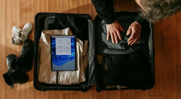 Osoba pakuje walizkę podręczną, w której widać ubrania, buty i tablet.