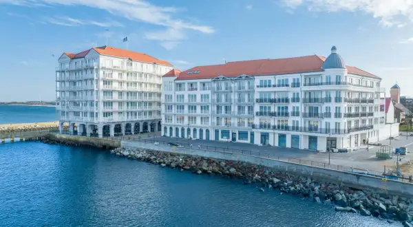 Nowoczesne apartamenty w Darłówku z wyżywieniem blisko morza. Białe budynki z czerwonymi dachami nad błękitną wodą.