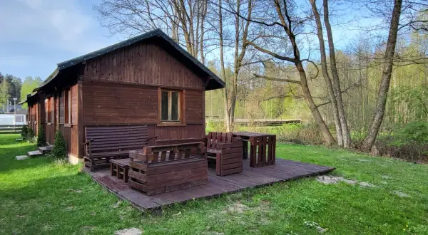 Drewniana chata z meblami na tarasie, otoczona zielenią i lasem. Idealne miejsce na agroturystykę w pobliżu.