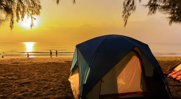 Namiot na polu namiotowym nad morzem przy plaży, gdzie słońce zachodzi, malując niebo na złoto.