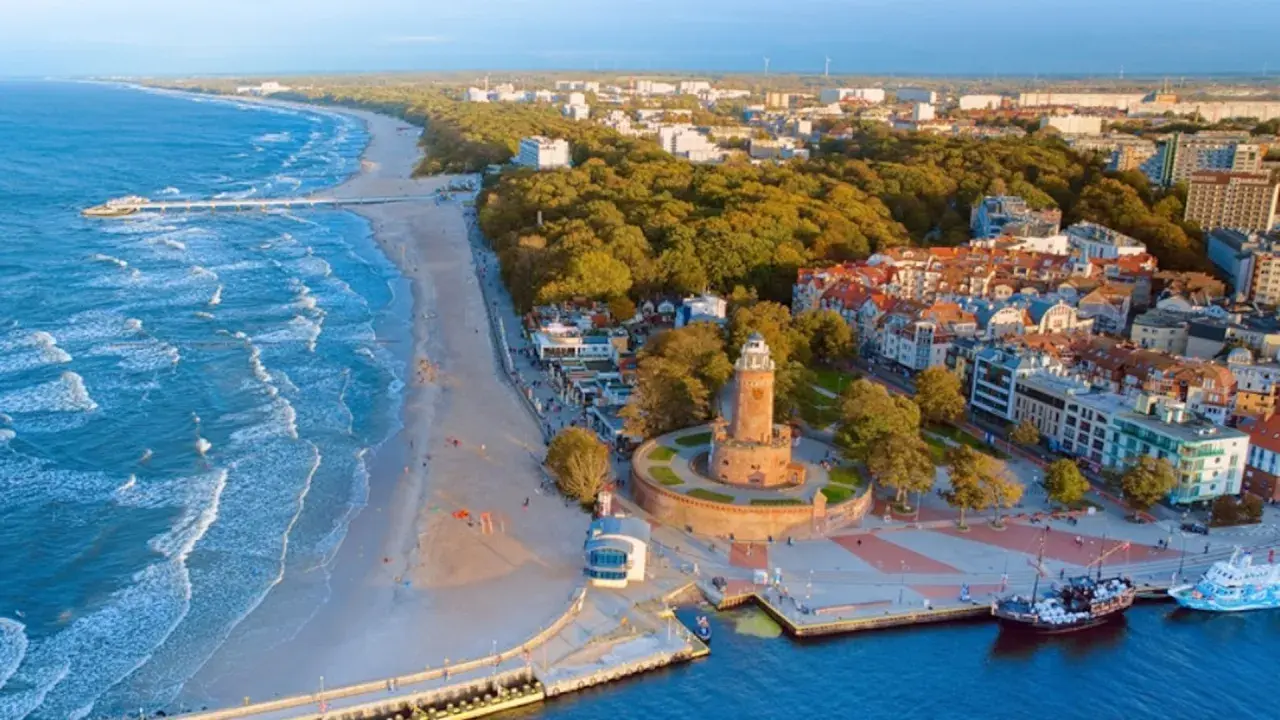 Widok na plażę, morze bałtyckie i latarnię morską. W tle hotel i zabudowania miejskie.