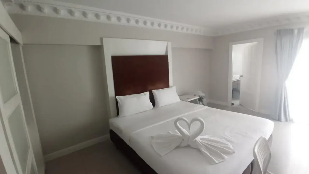 Elegancki pokój hotelowy z łóżkiem ozdobionym ręcznikami w kształcie łabędzi. Idealne miejsce, gdzie szukać noclegu na wakacje.