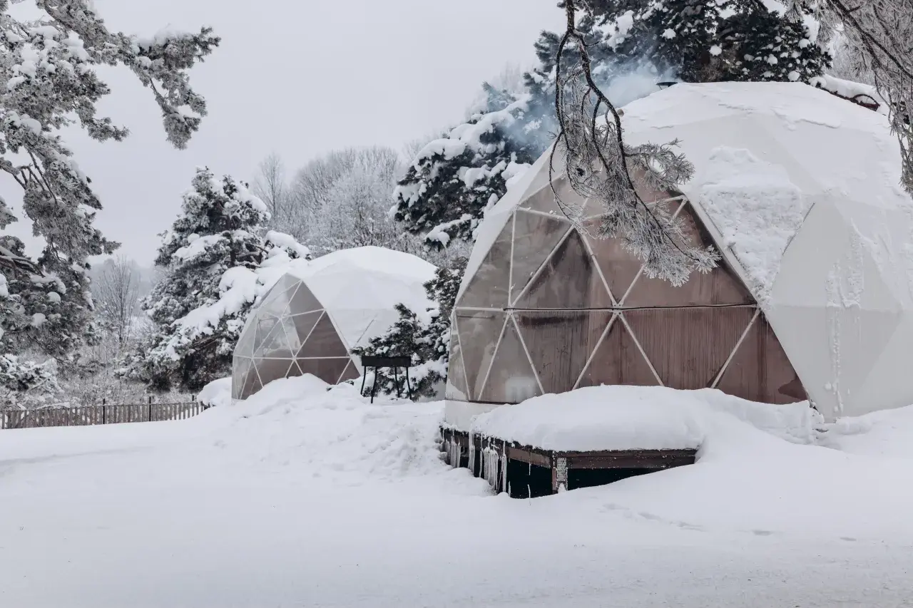 Śnieżne krajobrazy i przytulne domki do wynajęcia na weekend. Dym unosi się z komina jednego z igloo, zapraszając do środka.
