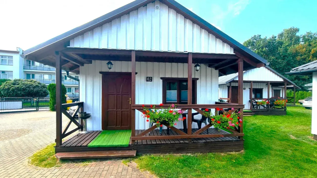 Urocze domki letniskowe Amber House z werandą i kwitnącymi pelargoniami. Idealne miejsce na wypoczynek.