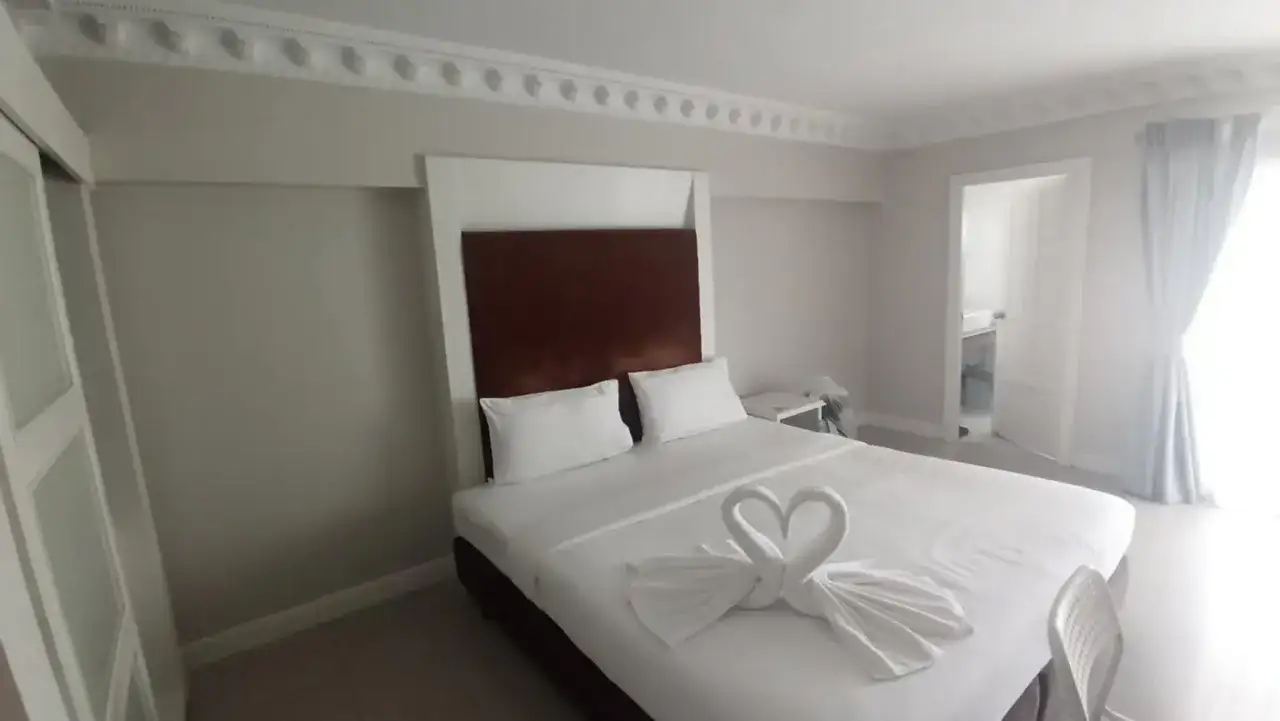 Elegancki pokój hotelowy z łóżkiem ozdobionym ręcznikami w kształcie łabędzi. Idealne miejsce, gdzie szukać noclegu na wakacje.
