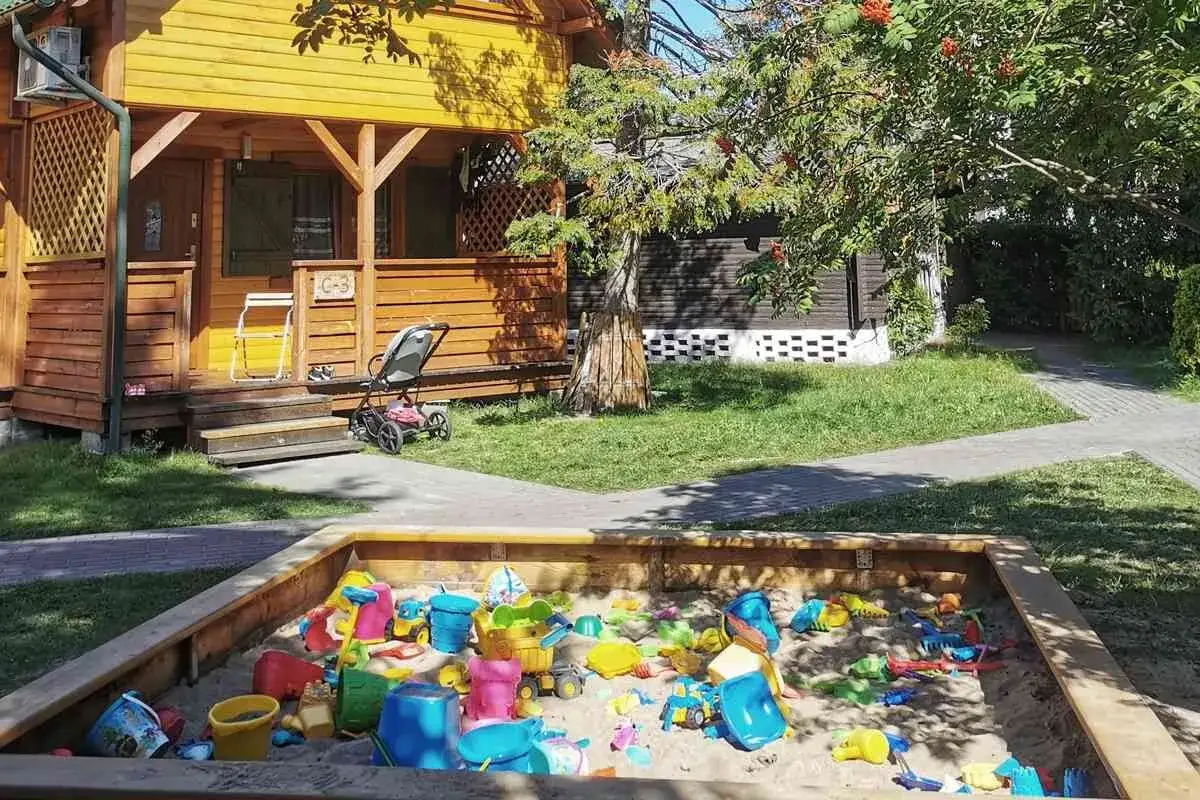 Piaskownica pełna zabawek czeka na dzieci w ośrodku wczasowym Sęk w Karwi. Obok drewniany domek i wózek.