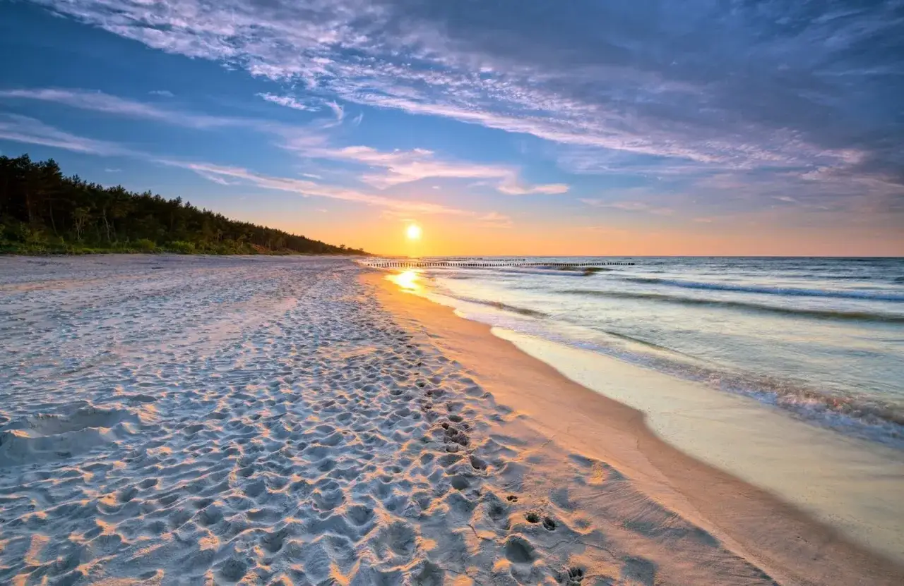 Zachód słońca nad morzem, piaszczysta plaża z ludzkimi śladami, las w tle. Idealne, fajne miejsce nad morzem dla dwojga.