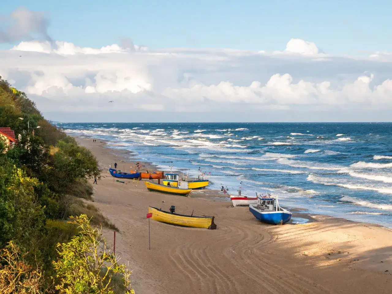 Wspaniała wycieczka nad morze! Kilka kolorowych łodzi rybackich na piaszczystej plaży, falujące morze i błękitne niebo z chmurami.