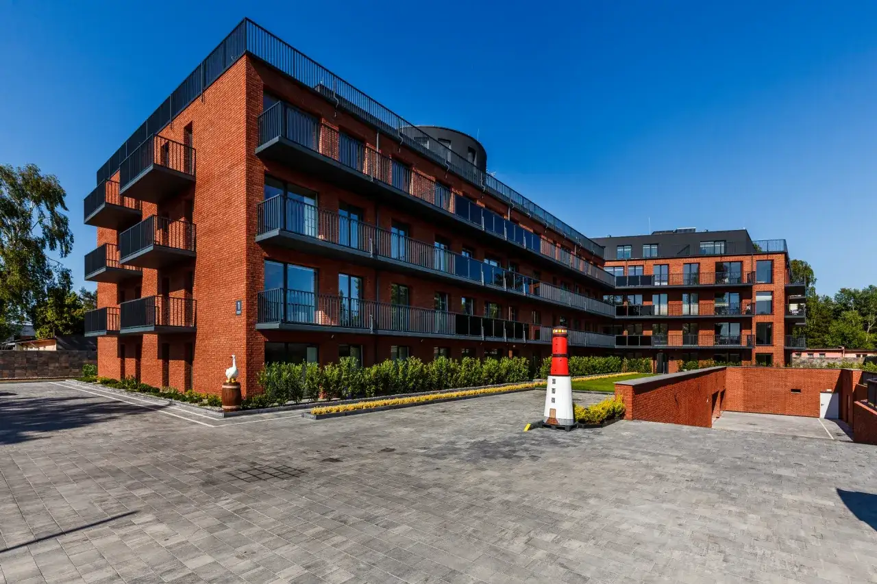 Nowoczesne apartamenty nad Bałtykiem z cegły, z balkonami i widokiem na morze. Przed budynkiem latarnia morska.