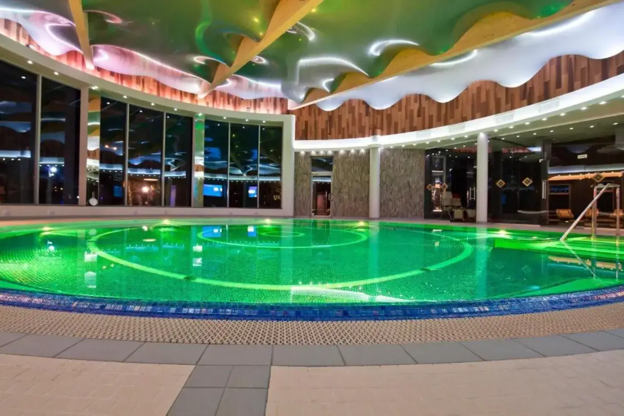 Nowoczesny basen z zielonym podświetleniem w hotelach nadmorskich Unitral. Falujący sufit i duże okna tworzą relaksującą atmosferę.