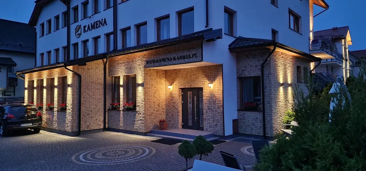 Ośrodek Kamena Karwia wita gości ciepłym blaskiem iluminacji. Elegancka fasada z cegły i nowoczesne oświetlenie tworzą przytulną atmosferę.