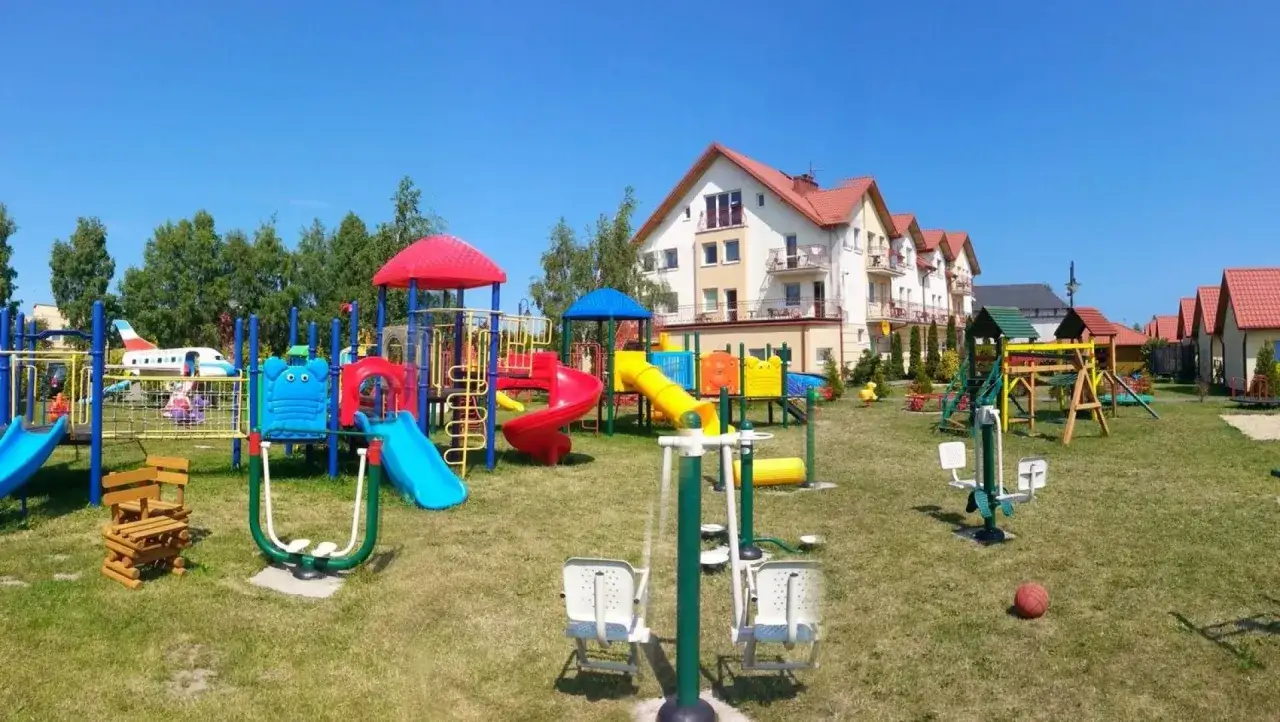 Kolorowy plac zabaw z samolotem i zjeżdżalniami. W tle budynki kompleksu wypoczynkowego Sedna.