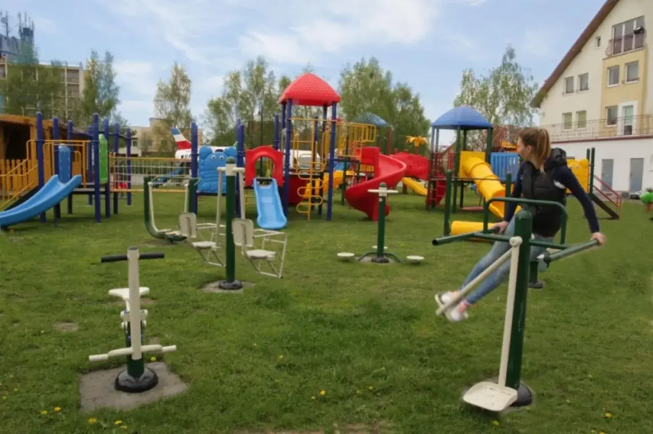 Kolorowy plac zabaw i siłownia plenerowa w kompleksie wypoczynkowym Sedna. Dziewczyna ćwiczy na urządzeniu.