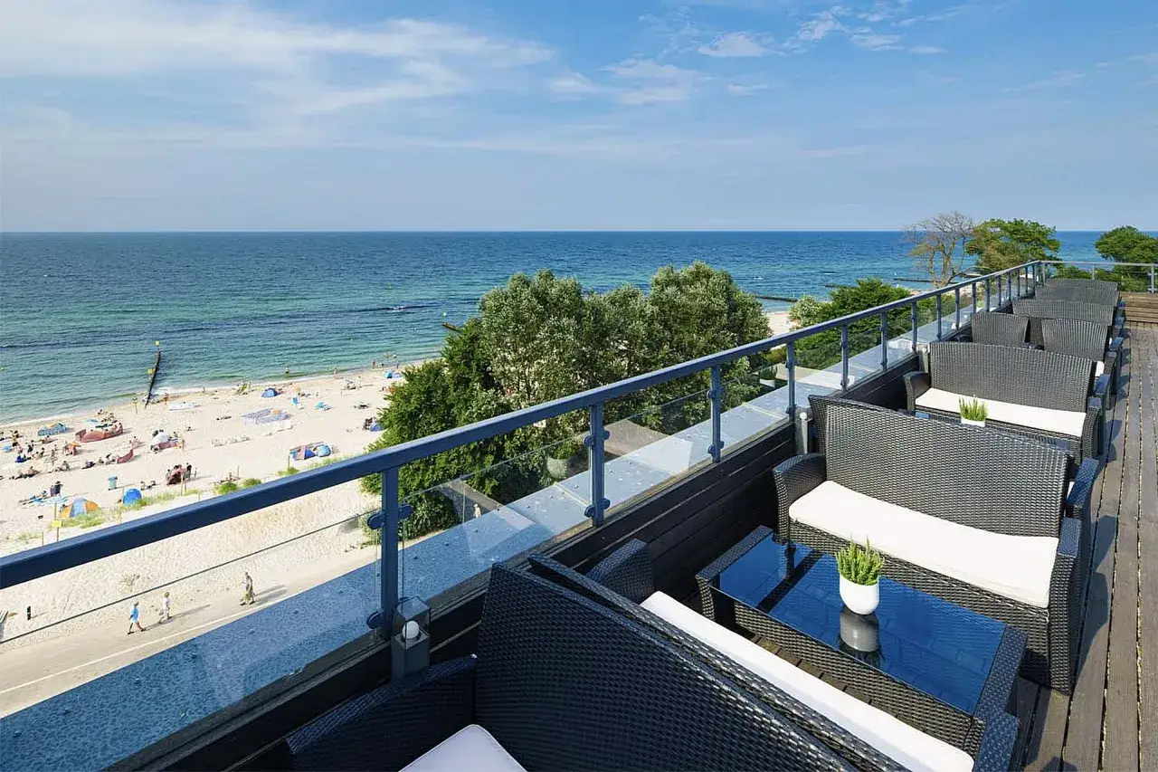 Relaks na tarasie hotelu nad samym morzem. Widok na piaszczystą plażę, turkusowe morze i błękitne niebo.
