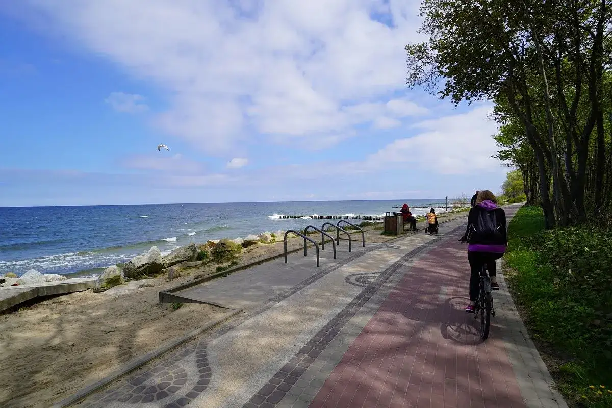 Sianożęty nad morzem: kobieta na rowerze jedzie ścieżką, w tle morze i plaża.